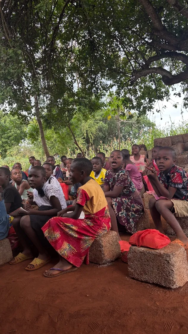 A group of children gathered together outdoors under trees in a rural community in Kilifi County, Kenya.